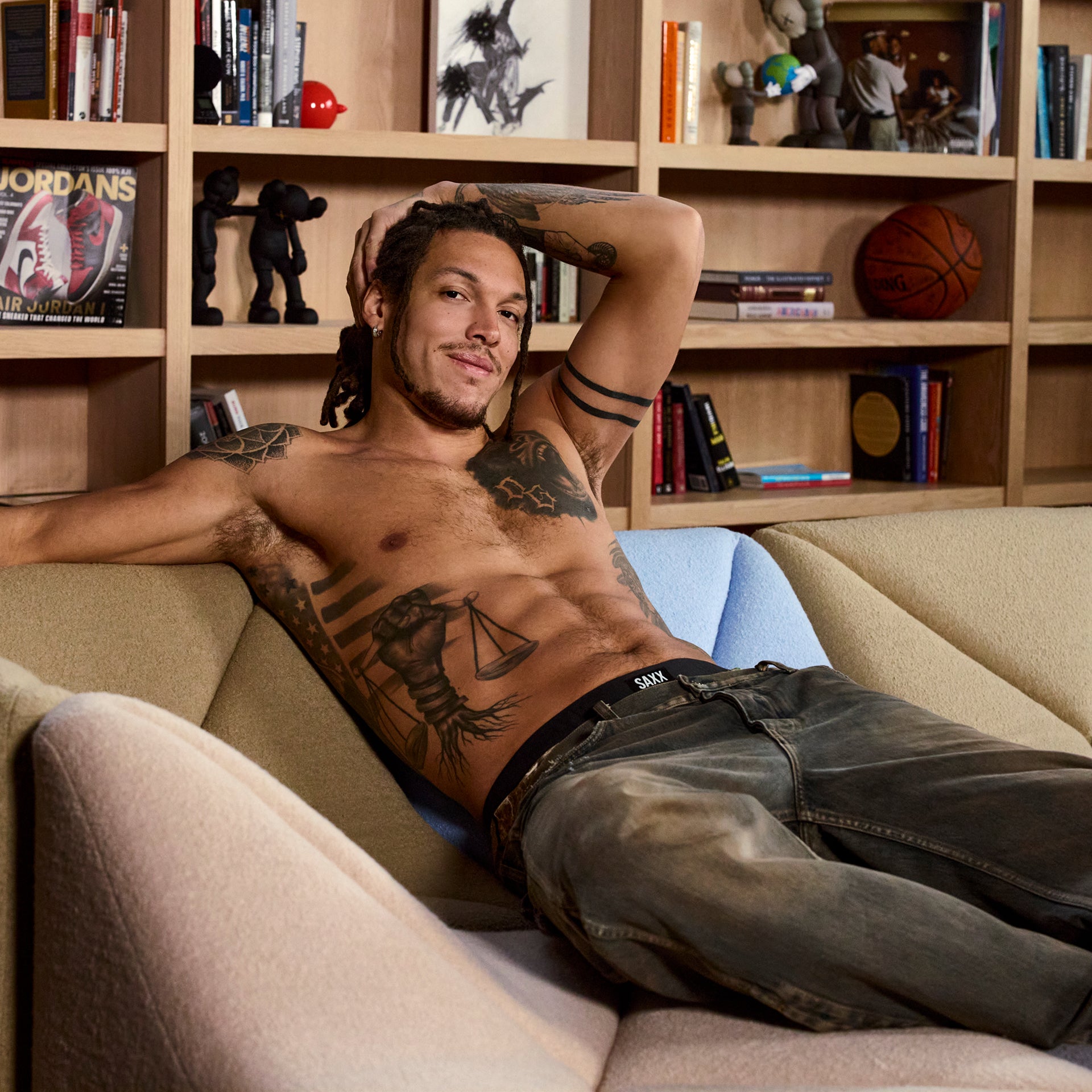 Pro Basketball Player and SAXX Gamechanger Aaron Gordon, lying on a couch in a room with bookshelves and sports memorabilia.