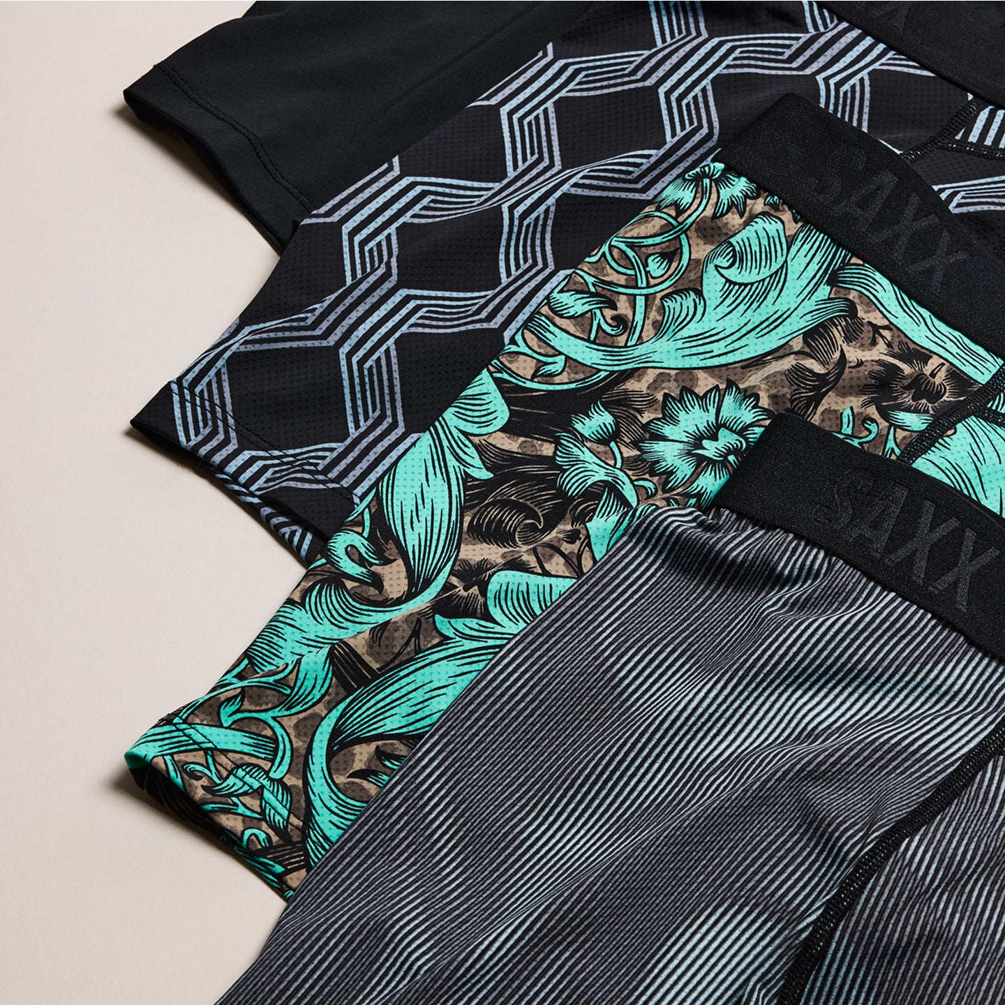 Three pairs of boxer briefs with different patterns on a beige background, featuring the brand 'Saxx'.